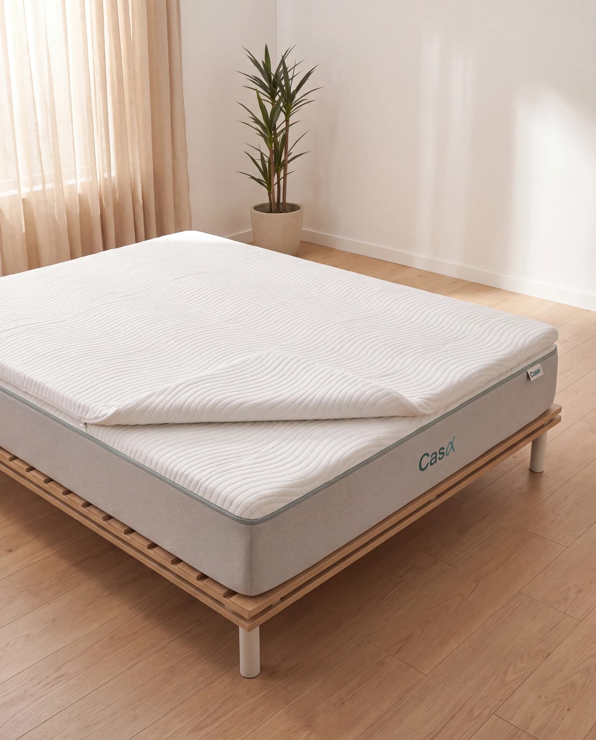 A thin white topper folded back at one corner on top of a Sync mattress in daylight.