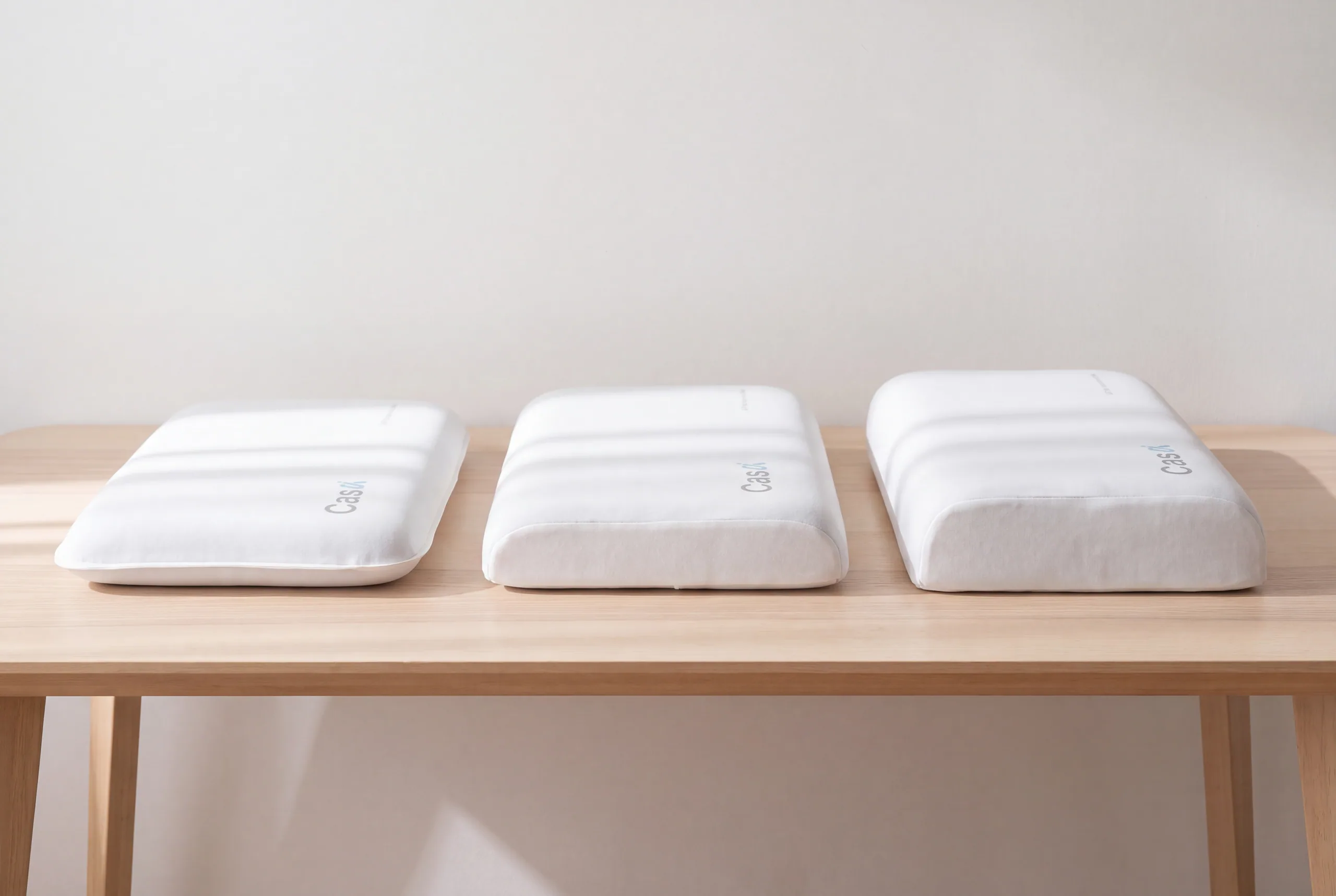 Three white contour pillows of 8, 10 and 12 cm height in a row, seen from the side.