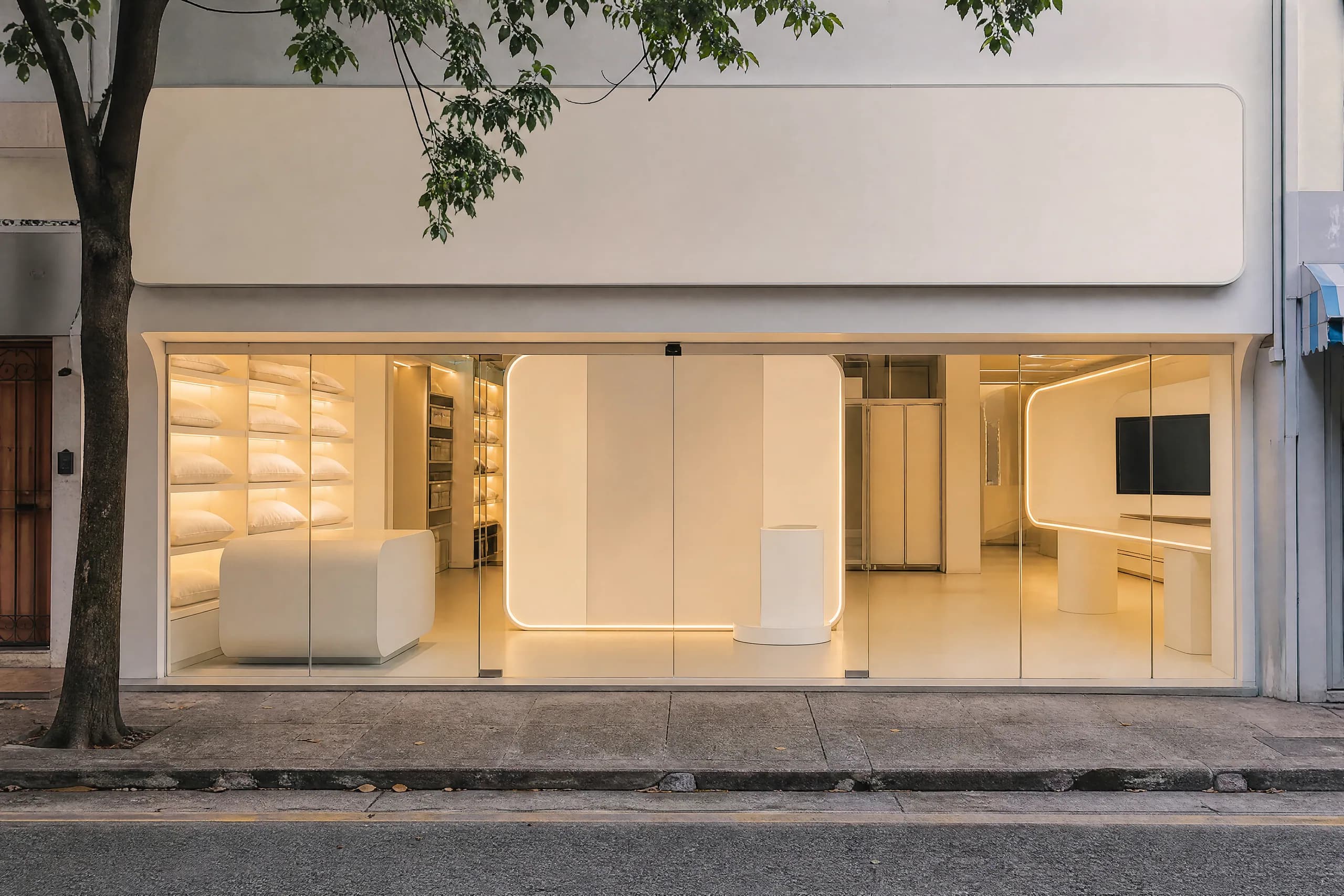 The glass shopfront of a sleep studio on Balestier Road in late afternoon, warm light inside and pillows on shelves.